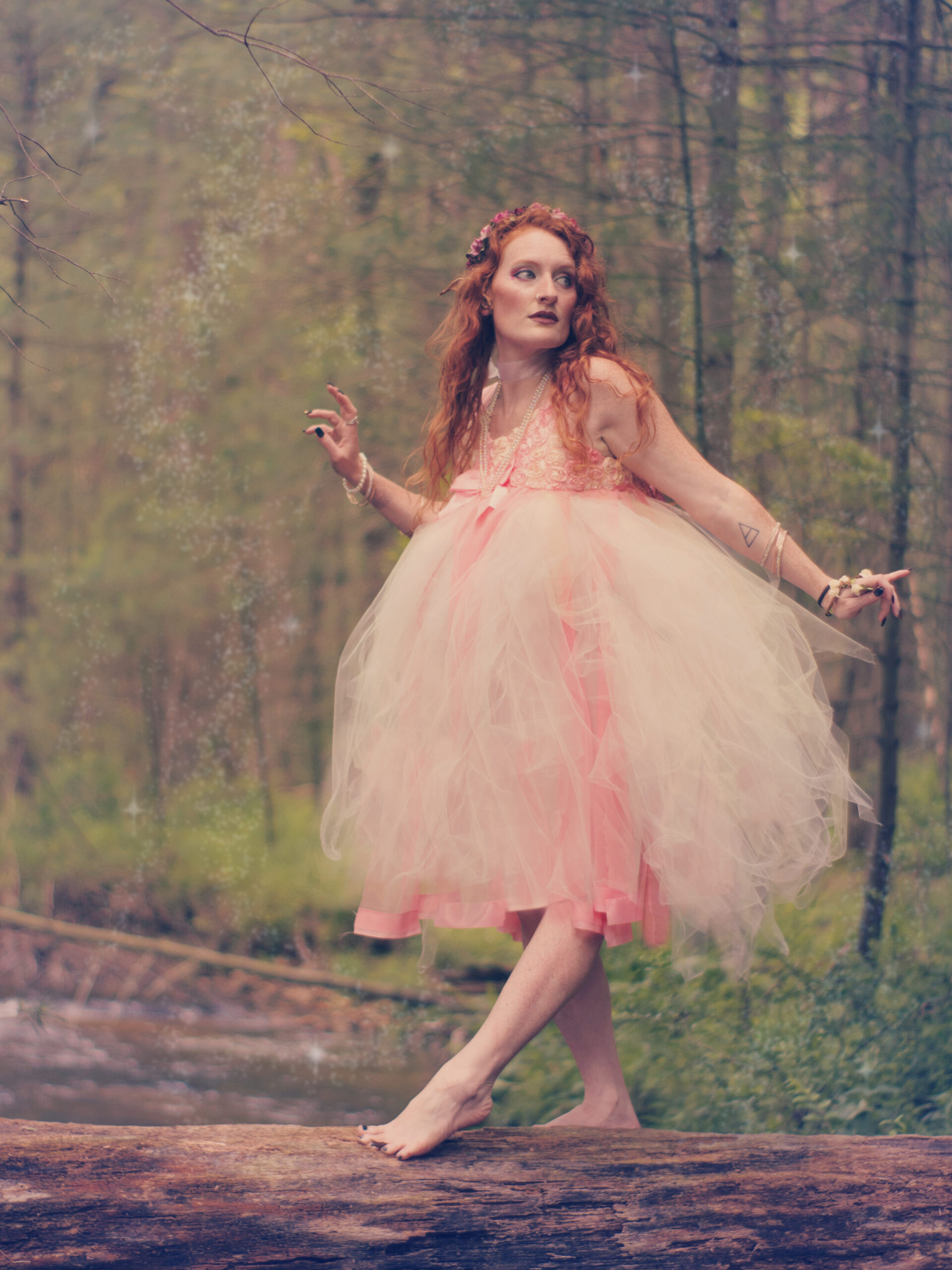 A fairy crossing a stream on a fallen log